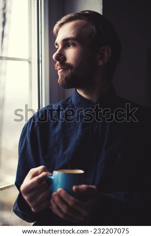 young guy drinking tea at the window