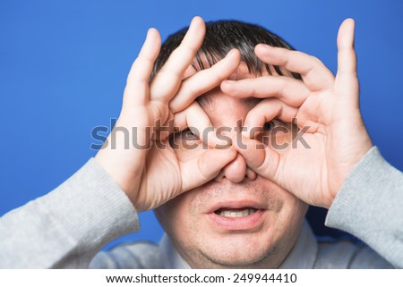 Funny young man with hand over eyes, looking through fingers