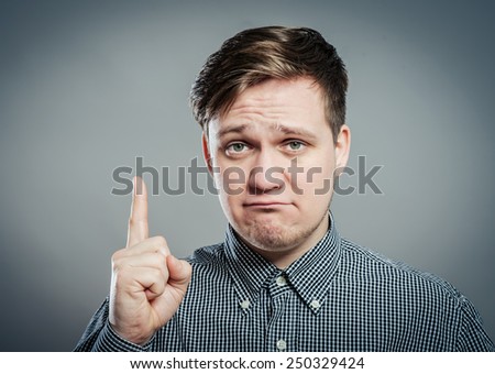 Portrait of disappointed young man pointing upwards while standing against gray background. Vertical shot.