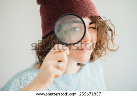 Woman in warm red winter hat and looking through the magnifying glass at blank copy space, over white