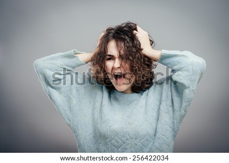 Frustrated stressed young woman. Headshot unhappy overwhelmed girl having headache bad day pulling her hair out isolated on grey wall background. Negative emotion face expression feelings perception