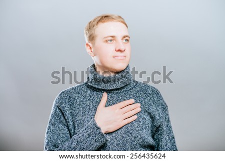 Young handsome man upset keeps his heart, hands on heart. Gesture. On a gray background