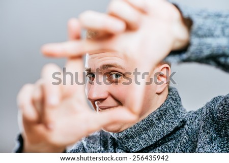 Handsome blond  young man doing frame gesture with fingers, looking at camera through it