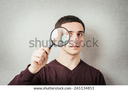 Man with magnifying lens over grey background. / Portrait of a normal man looking camera.