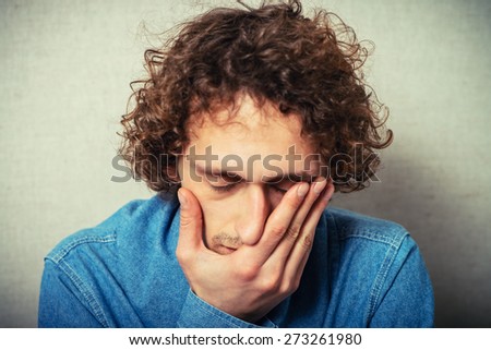 Curly young man crying, sad, covered his face with his hands. On a gray background