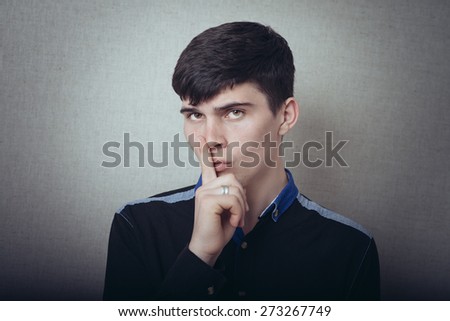 A man holding a finger to his mouth, a gesture silence, too loud. On a gray background.
