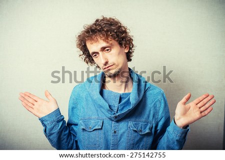Curly man showing a gesture I have nothing, I did not, empty hands to the sides. On a gray background.