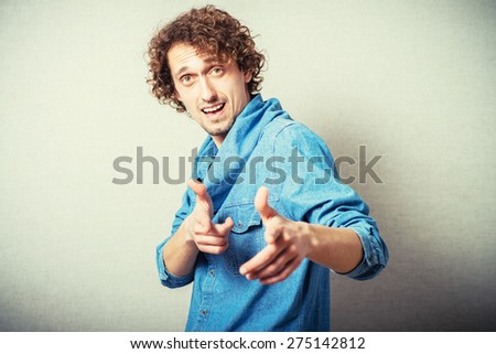 Curly man index finger at the camera. On a gray background.