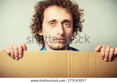 Curly man with empty cardboard. On a gray background.