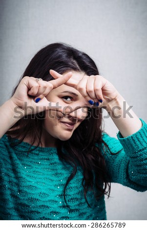 Young happy woman holding her hand over her eye as glasses and  looking through fingers