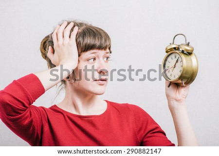Woman looking at the alarm clock with the hand on his head. On a gray background.