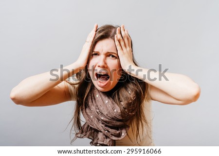 Young woman screams hands on his head. On a gray background.
