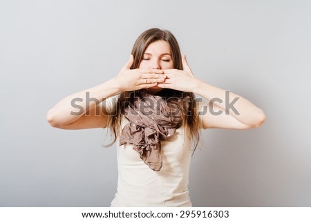 Young woman closed her eyes and covered her mouth with her hands. On a gray background.