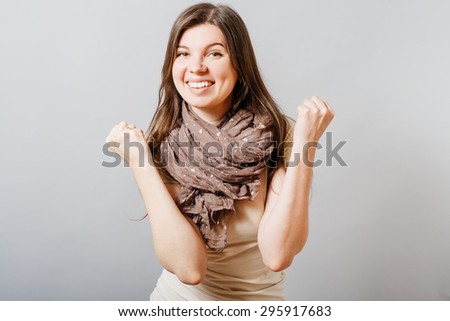 Young woman shows gesture of victory, joy, success. On a gray background.