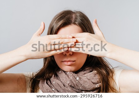 Young woman covering her eyes with his hands. On a gray background.