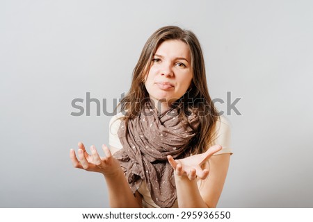 Young woman unhappy asks what you want. On a gray background.