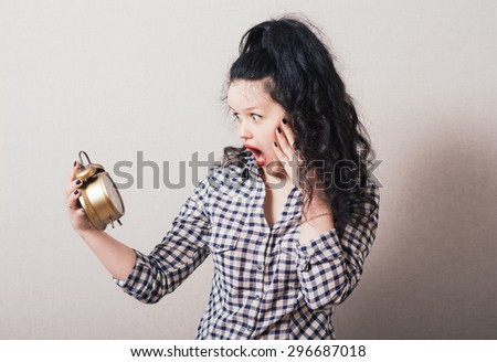 Woman looking at the alarm clock in her hand. On a gray background.