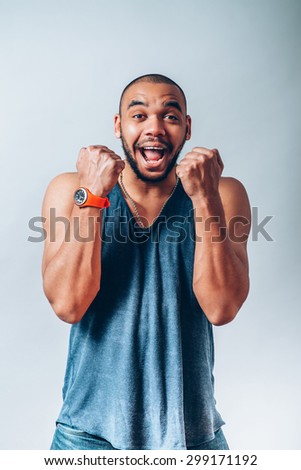 African man smiling happy victory, hands it upwards with his fists. On a gray background.