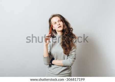 Young girl thinking with a pencil in the head. On a gray background.