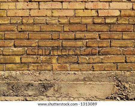 An orange and yellow brick wall ending on a concrete foundation.