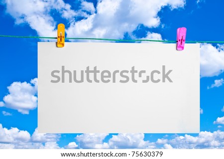 Empty blank paper on the clothes pegs against blue sky. billboard.
