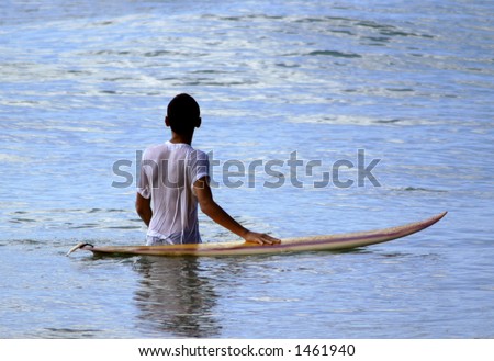 young man with hand on surfboard looking out to sea.