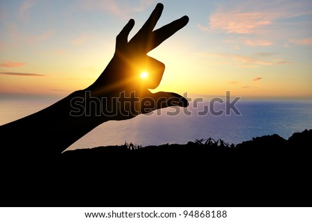 silhouette of a human hand on the background of the sea beach, through the fingers of which the sun shines brightly