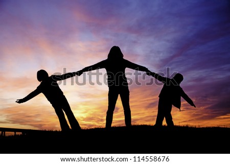 A mother holds her two children while playing during sunset.