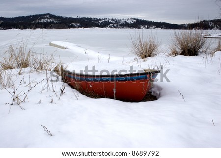 A snow filled boat by a frozen lake.