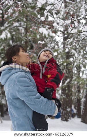 A mother and her son look up at snow covered berries in a tree.