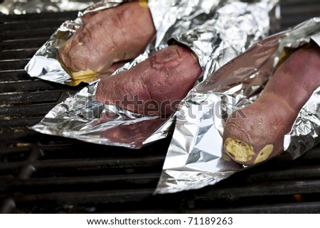 Cooking sweet potatoes wrapped in tin foil over a gas grill.
