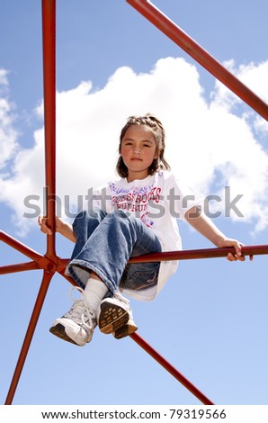 A cute young girl climbs up high on a jungle gym at a playground.