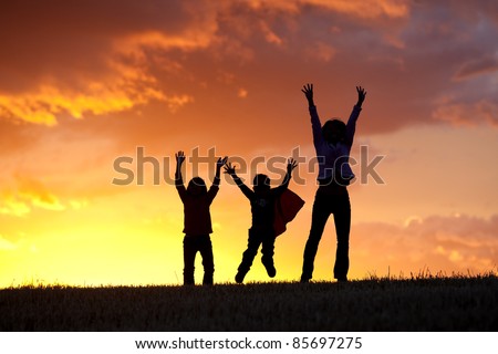 A woman and her two kids jump for joy at sunset.