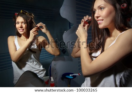 Beautiful woman curling her hair with roller and looking in mirror