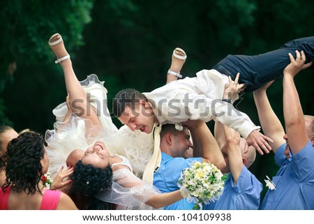 A happy groom and bride  tossed into air by a group of friends