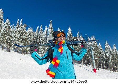 Young male skier holding ski; blue jacket; black pant; horizontal orientation