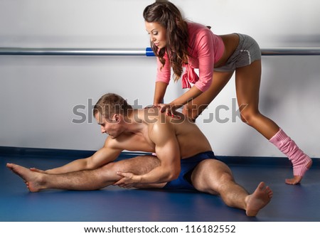 Female trainer helping guy to siting on straddle split on floor in dance studio
