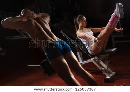 Young bodybuilder training his muscular back and woman working on her prelum on the bench in gym