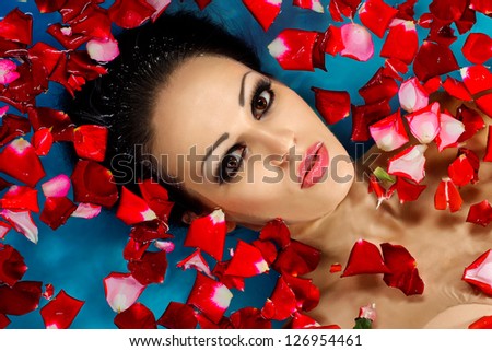Face of pretty woman floating in swimming pool with petals of rose