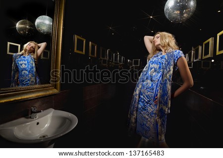 Young blonde woman in front of mirror in the restroom with disco mirror ball