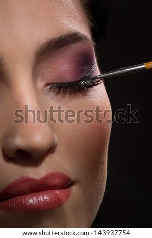Sexy brunette putting mascara makeup in darkness