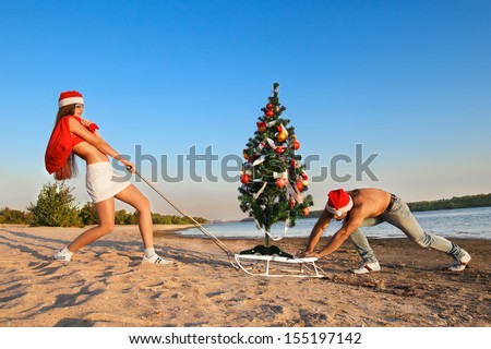 Sexy Santa pulling Christmas tree on a sled at the beach.  (concept: Tropical winter fun)