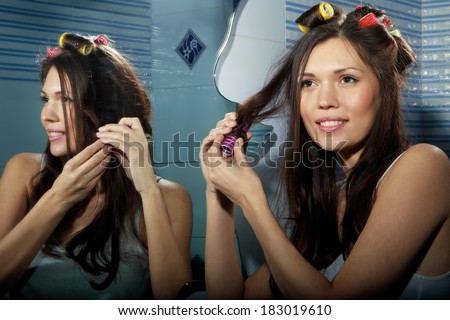 Beautiful woman curling her hair with roller and looking in mirror