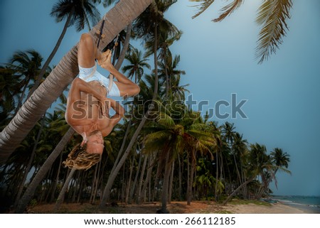 Muscular man doing upside down yoga on palm tree