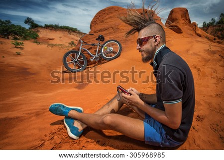 Biker take a rest and listen music on road in the high mountains of sand dunes . Background blue sky with clouds