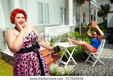 Plus size curly red hair smiling woman watering hose  plant and her sister is reading book