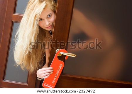 Sexy woman smiling, looking from behind the door, holding hotel sign \