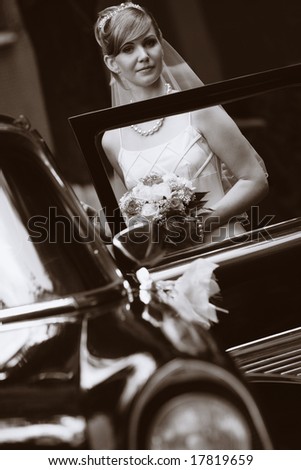 Sepia image of bride standing aside luxury wedding car