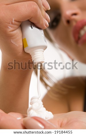 Pretty girl pressing plastic tube with cosmetic cream onto palm