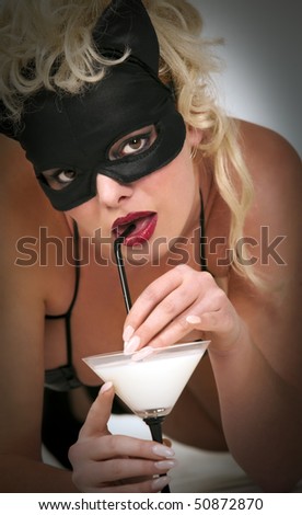 Portrait of the blond model wearing black cat, licking - drinking milk from the martini glass